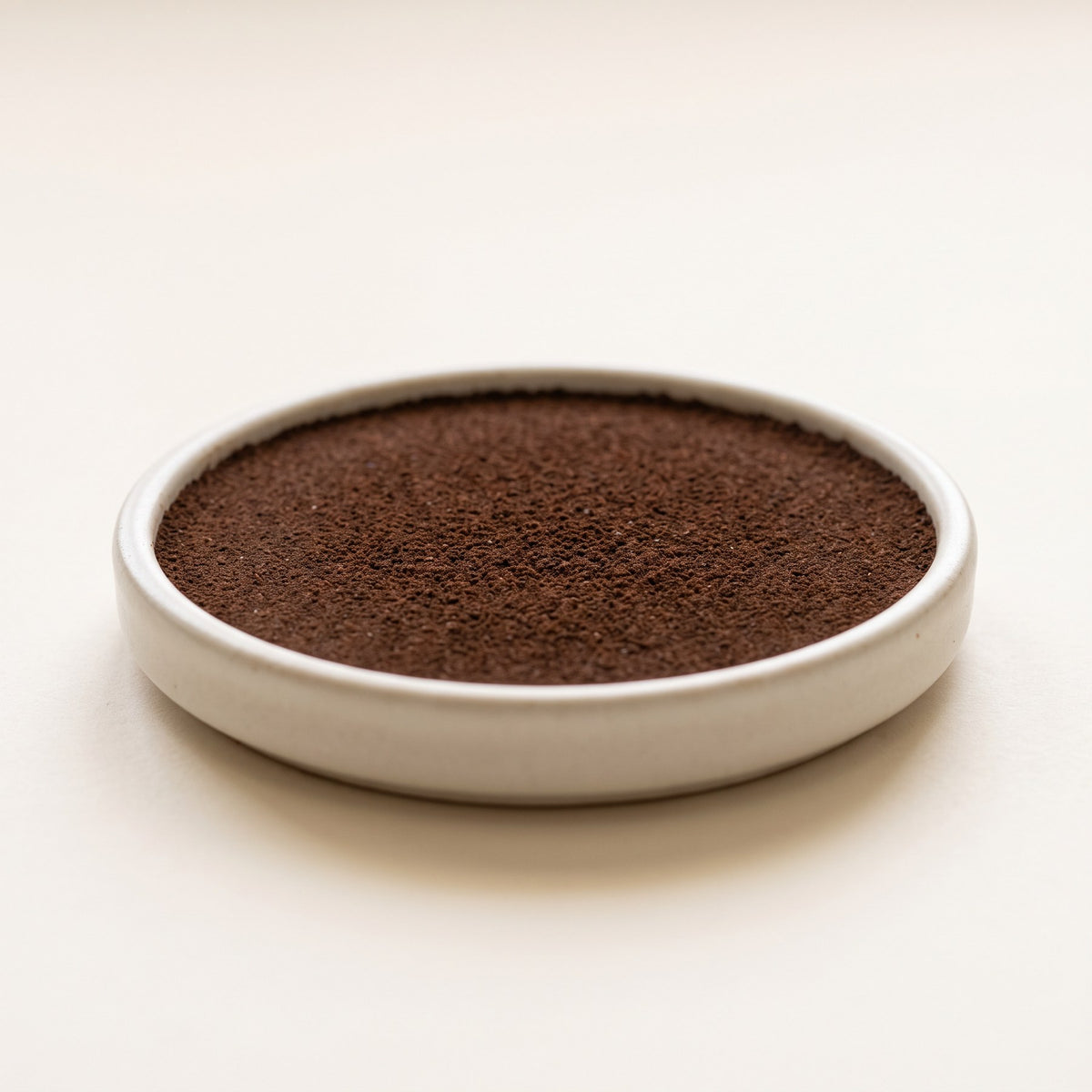 Evenly leveled flat disc of fine espresso grounds in a shallow dish