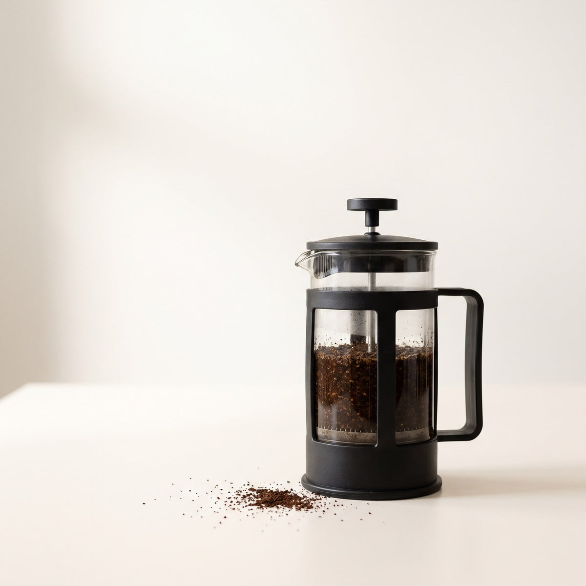 Glass French press with coarse coffee grounds, plunger raised