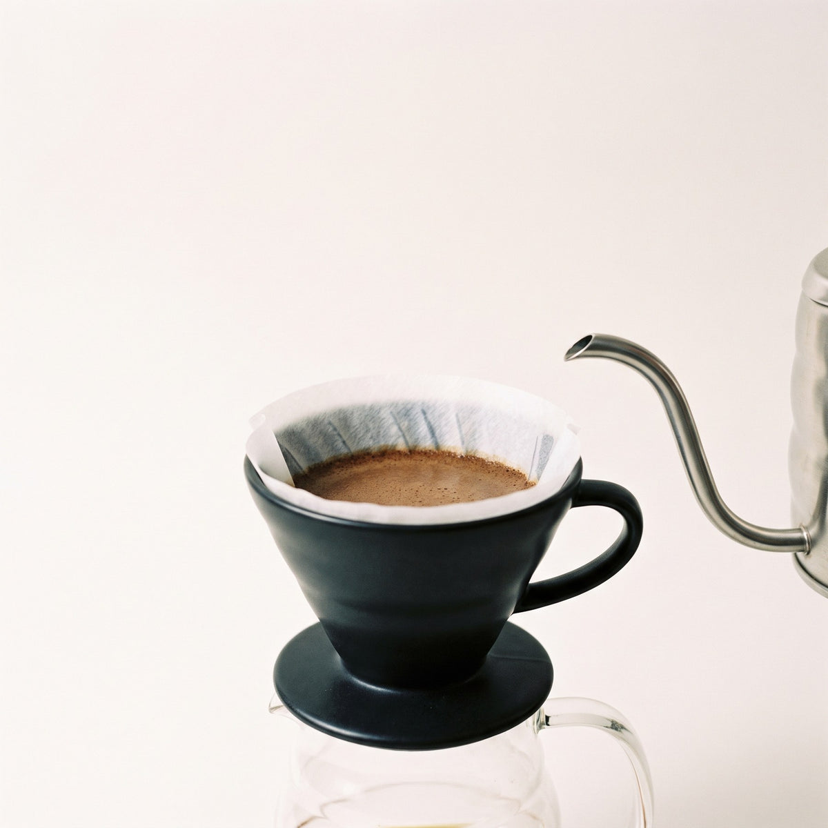 Ceramic pour over dripper with a bed of medium ground coffee and a gooseneck kettle