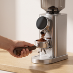 Hand clipping a portafilter into the cradle of the BioloMix CG210 coffee grinder