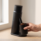 Hand lifting the magnetic grounds cup from under the chute of the CAFOVO G1048C