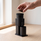 Hand lifting the walnut lid of a black CF Wisdom portable grinder