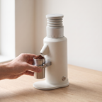 White GZZT GF64 espresso grinder on a wooden counter, hand removing the stainless dosing cup
