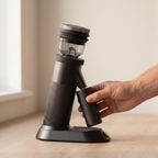Hand lifting the grounds cup from the cradle of the HiBREW G5 coffee grinder