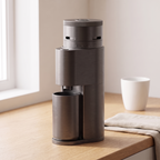 Graphite grey SIMELO Alien portable grinder on a wooden counter beside a cup