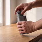 Hands holding a graphite grey SIMELO Alien portable grinder over a wooden table