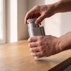Hands separating the grounds cup from a silver SIMELO Alien grinder
